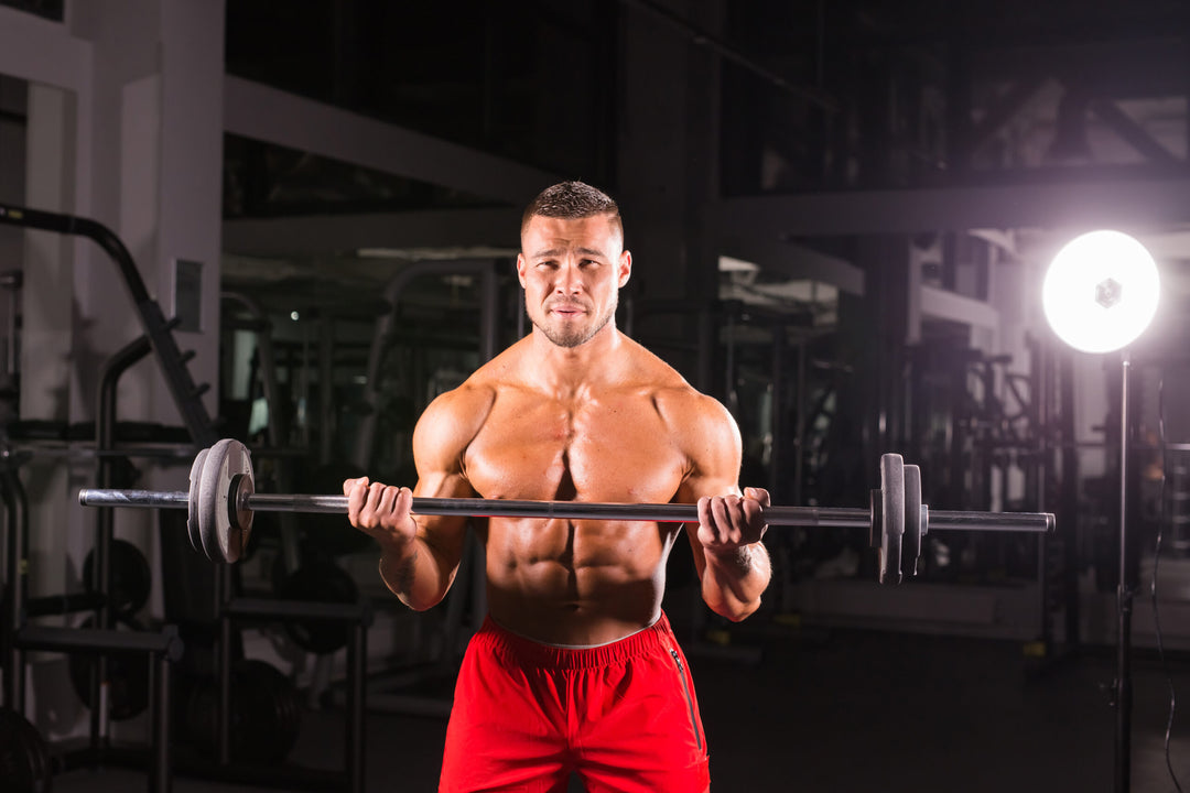 Bodybuilder doing the exercises with barbell. Strong male with naked torso on dark background. Strength and motivation.